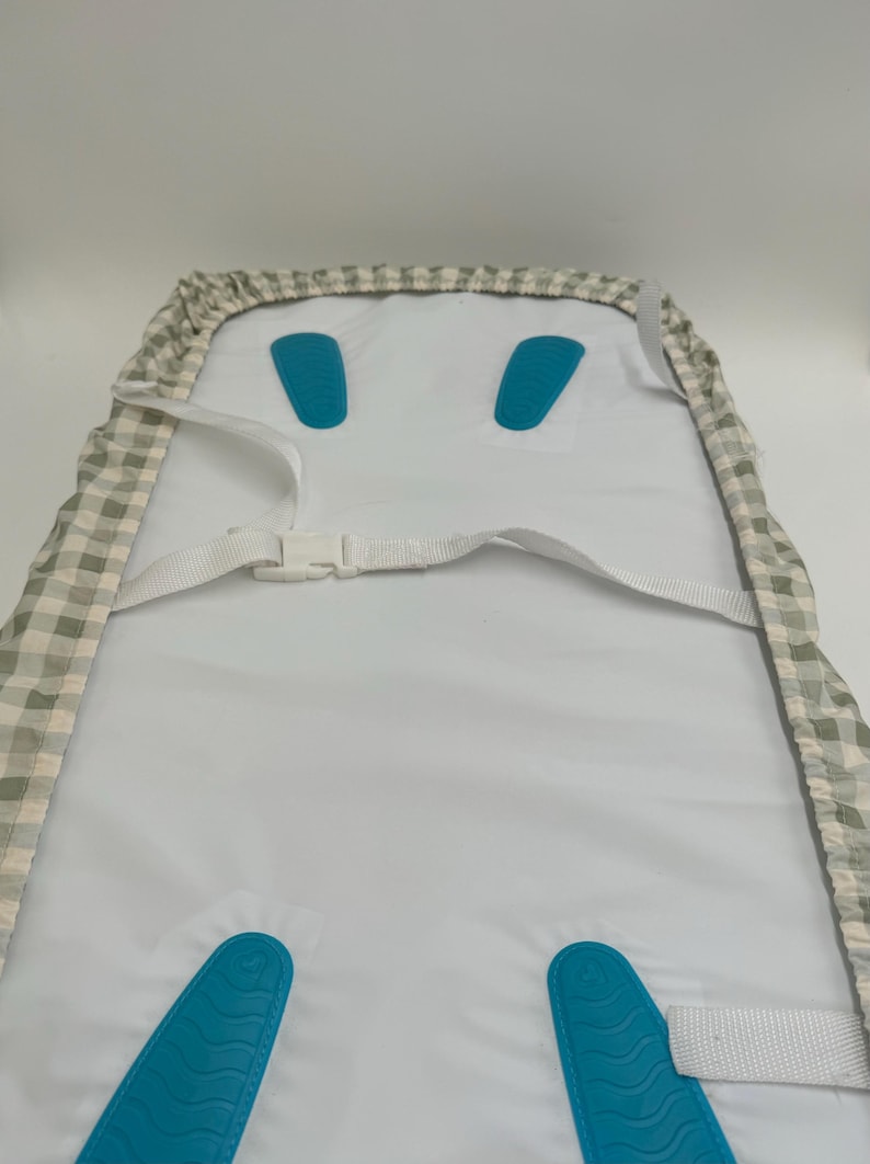 May include: A white high chair cover with a grey and white checked pattern. The cover has two blue straps with buckles and two blue padded inserts.