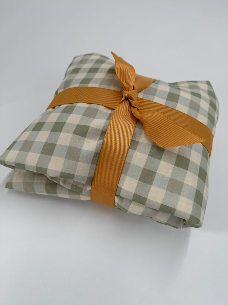 May include: A green and white gingham fabric gift wrapped with a golden ribbon.