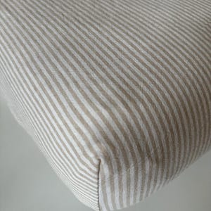 May include: A close-up of a beige and white striped fabric. The fabric has a subtle sheen and a smooth texture.