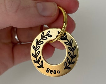 May include: Gold-colored metal keychain with a round tag engraved with a wreath of leaves and the name "Beau".
