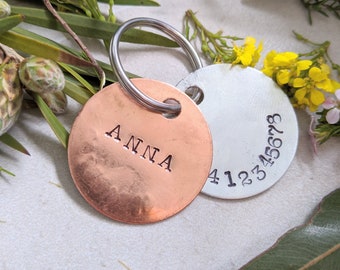 May include: Two round metal keychains. One is copper and engraved with the name "ANNA". The other is silver and engraved with the numbers "412345678".