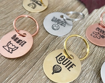 May include: Six round metal keychains with different designs and names. The keychains are in various colors, including gold, silver, and copper. The names on the keychains are Basil, Louiie, Luna, and a flower design.