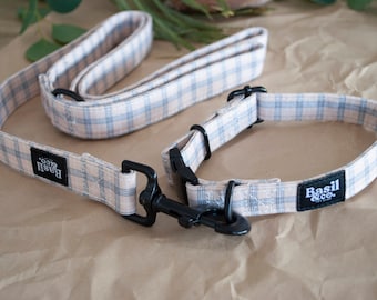 May include: A pink and blue plaid dog collar and leash set with black hardware and the Basil & Co. logo.