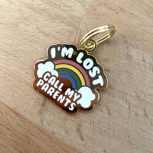 May include: Gold-coloured metal keychain with a rainbow and clouds design. The text "I'm Lost Call My Parents" is printed on the keychain.