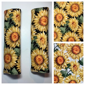 K&ouml;nnte beinhalten: Zwei schwarze Sitzgurtschoner aus Stoff mit Sonnenblumenmuster. Der Stoff hat einen schwarzen Hintergrund mit gelben Sonnenblumen und gr&uuml;nen Bl&auml;ttern.