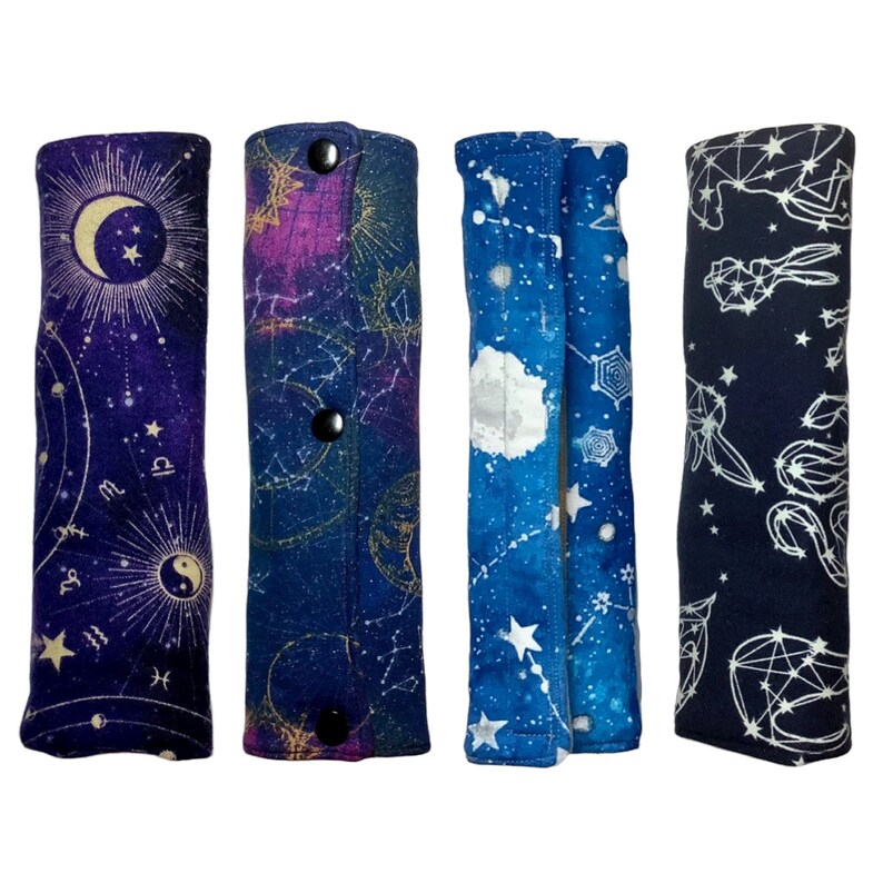 May include: Four fabric pencil cases with a celestial theme. Each case features a different constellation pattern in shades of blue, purple, and white on a dark background. The cases have a button closure.