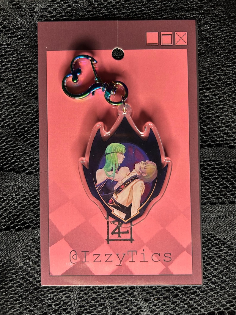 May include: A clear acrylic keychain with a colorful iridescent clasp. The keychain features a stylized image of two figures with green and blonde hair. The background is a dark blue with a pink and red card backing. The text "@IzzyTics" is visible.