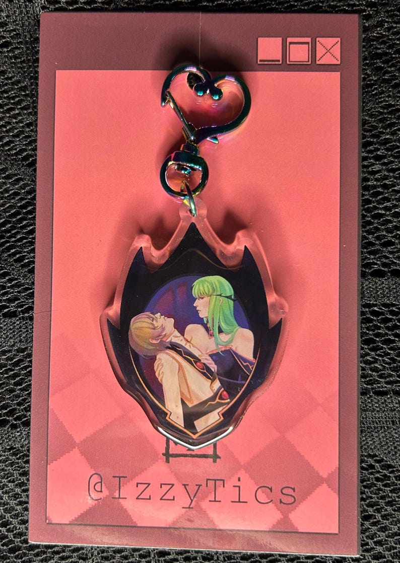 May include: A clear acrylic keychain with a heart-shaped clasp. The keychain features a colorful illustration of two anime characters. The background is a pink card with a checkered pattern and the text "@IzzyTics".