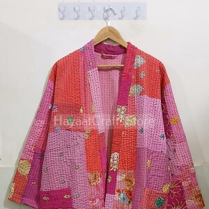 May include: A pink and red patchwork kantha quilt robe with floral embroidery. The robe has a long, flowing silhouette and is perfect for layering over clothing.