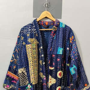 May include: A long-sleeved navy blue jacket featuring a patchwork design with white kantha stitching. The garment is adorned with various colorful embroidered floral patterns, gold-toned metallic fabric accents, and circular decorative motifs.