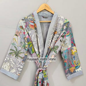 Puede incluir: Una bata gris de patchwork con un diseño floral y paisley. La bata tiene mangas largas y un cierre de lazo. El texto "Hayaat Crafts Store" es visible en la bata. La bata está colgada en una percha de madera.