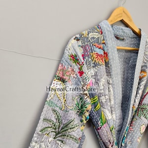 May include: A gray, floral-patterned robe with a light blue trim, hanging on a wooden hanger. The robe features a patchwork design with images of flowers, leaves, and animals. The text "HayaaCraftsStore" is visible on the robe.