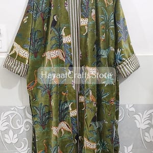 K&ouml;nnte beinhalten: Olivgr&uuml;ner Samtrobe mit Dschungel-Print mit Leoparden, Tukanen und Palmen. Die Robe hat gestreifte Manschetten und ein gestreiftes Innenfutter. Der Text "Hayaat Crafts Store" ist auf der Robe zu sehen.