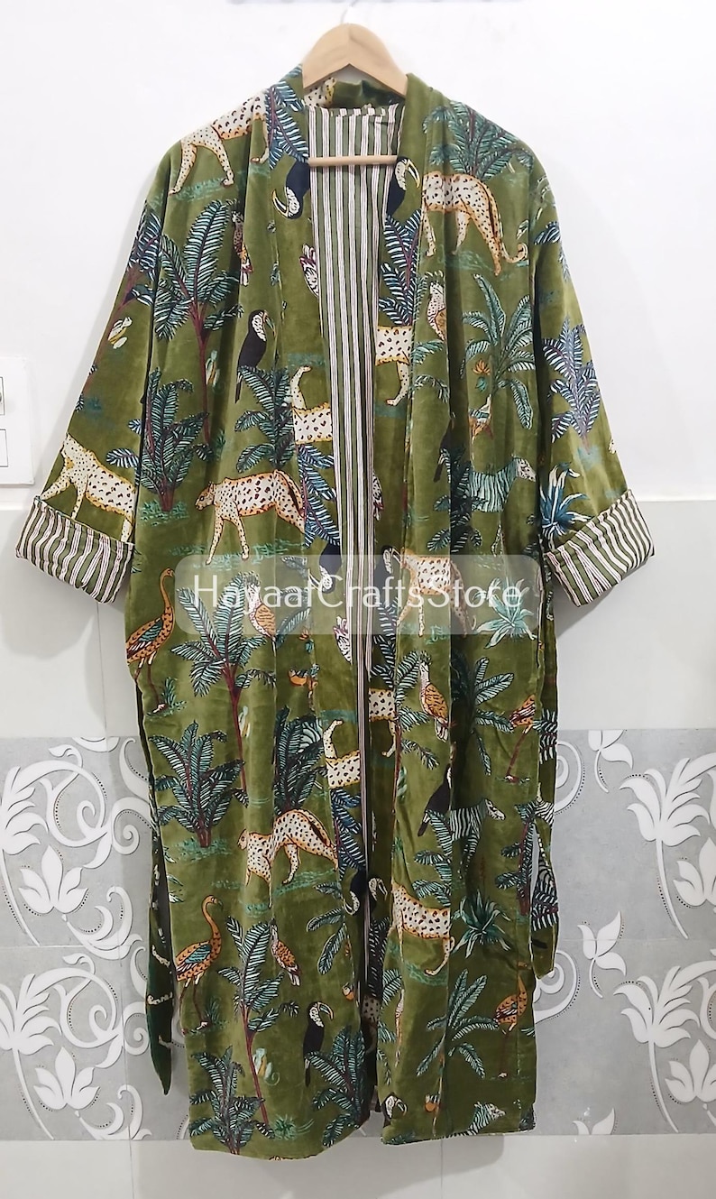 K&ouml;nnte beinhalten: Olivgr&uuml;ner Samtrobe mit Dschungel-Print mit Leoparden, Tukanen und Palmen. Die Robe hat gestreifte Manschetten und ein gestreiftes Innenfutter. Der Text "Hayaat Crafts Store" ist auf der Robe zu sehen.