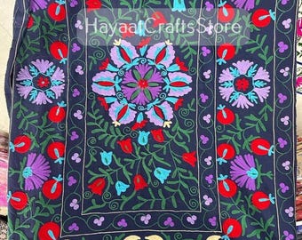 May include: A dark blue textile featuring intricate multi-colored floral embroidery in red, purple, and light blue. The design includes a central mandala-like motif surrounded by repeating flower patterns and vines. The text HayaatCraftsStore is visible.