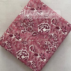 May include: Pink cotton fabric with a white floral print. The fabric features a repeating pattern of roses and leaves.