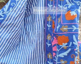 May include: A blue cotton jacket with a striped lining and colorful floral embroidery. The jacket has a tie closure and a pocket on the front. The text "Hayaat Crafts Store" is visible on the jacket.
