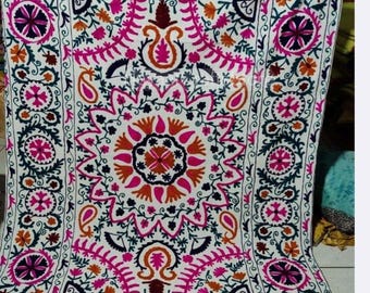 May include: A white textile featuring intricate hand-stitched embroidery in vibrant shades of magenta, dark purple, and orange. The design includes a large central floral medallion surrounded by paisley motifs, scrolling vines, and circular borders.