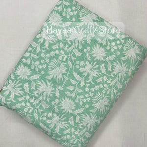 May include: A green fabric with a white floral pattern. The fabric has a soft, natural feel and is perfect for crafting projects.