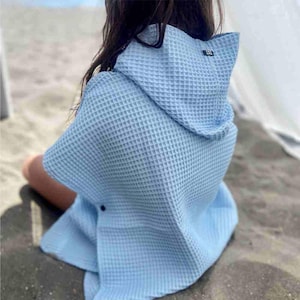 Könnte beinhalten: Ein hellblaues Waffelgewebe-Handtuch mit Kapuze und einem schwarzen Etikett. Das Handtuch ist aus weichem, saugfähigem Material und perfekt zum Abtrocknen nach dem Schwimmen oder Duschen.