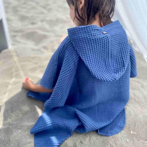 Könnte beinhalten: Ein blaues Waffelgewebe-Kapuzenhandtuchponcho für Kinder. Das Poncho hat eine Waffelstruktur und eine Kapuze.