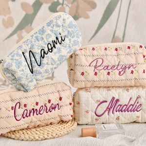 Puede incluir: Cuatro neceseres acolchados personalizados. Uno es azul claro con un estampado floral y el nombre "Naomi" en escritura negra. Los otros tres son de color crema con estampados florales y a rayas, cada uno bordado con un nombre en cursiva.