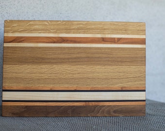 May include: A rectangular wooden chopping board with a multi-toned wood grain pattern. The board has a light brown, dark brown, and black striped design.