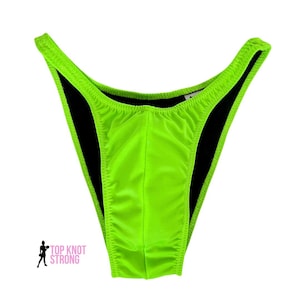 May include: Lime green swimsuit with a black lining. The swimsuit has a low cut and a high leg.
