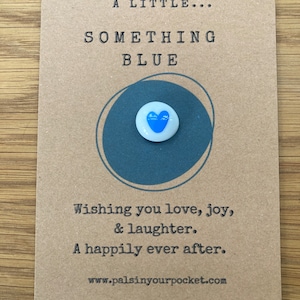 May include: A small card with the text "A Little... Something Blue" and a blue heart charm. The card also includes the text "Wishing you love, joy, & laughter. A happily ever after." and the website address "www.palsinyourpocket.com".