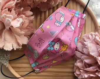 May include: Pink face mask with a repeating pattern of a cartoon character with a bow and a pink dress. The character is surrounded by stars, candy canes, and other colorful designs.
