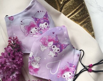 May include: Two purple and white fabric face masks with a cartoon character design. The masks feature a heart shape and a cartoon character with a star on their head. The masks are on a white surface.