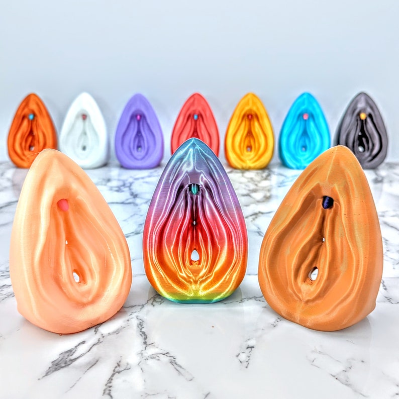 May include: A collection of colorful ceramic sculptures in various shapes and sizes. The sculptures are arranged in a semi-circle on a white marble surface. The sculptures are all abstract and feature a variety of colors, including pink, blue, orange, and purple.