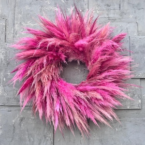 May include: A pink pampas grass wreath, a popular choice for home decor, hangs against a gray wall.