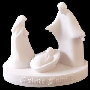 Peut inclure: Figurines en céramique blanche représentant la Sainte Famille. Les figurines sont stylisées et simples, avec l'enfant Jésus couché dans une crèche. La base de la figurine est inscrite des mots "Sainte Famille".