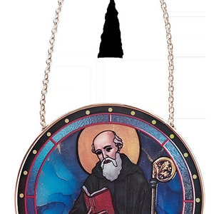 Puede incluir: Un adorno redondo de vitral para ventana que representa a un santo sosteniendo un libro y un bastón. El santo lleva una túnica marrón y tiene barba blanca. El fondo es un diseño de vitral azul y rojo.