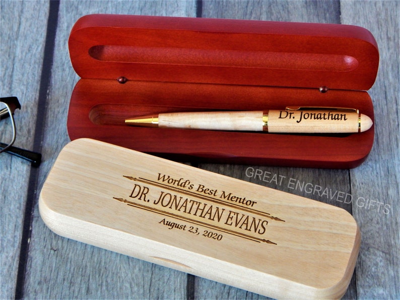 May include: A wooden pen and case set. The pen is light-colored with gold accents and the inscription "Dr. Jonathan." The case is open, revealing a red interior. The closed case is engraved with "World's Best Mentor DR. JONATHAN EVANS August 23, 2020."