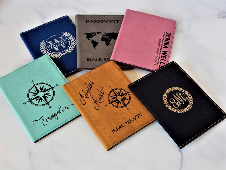 May include: Six passport holders with different designs. The holders are made of leather and have different colors, including blue, brown, pink, black, and green. The holders are personalized with names, initials, and compass designs.