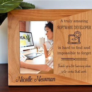 May include: A wooden picture frame with a photo of a person at a computer, holding a mug. The frame has engraved text: "A truly amazing SOFTWARE DEVELOPER is hard to find and impossible to forget." It also includes the name "Nicolle Newman".