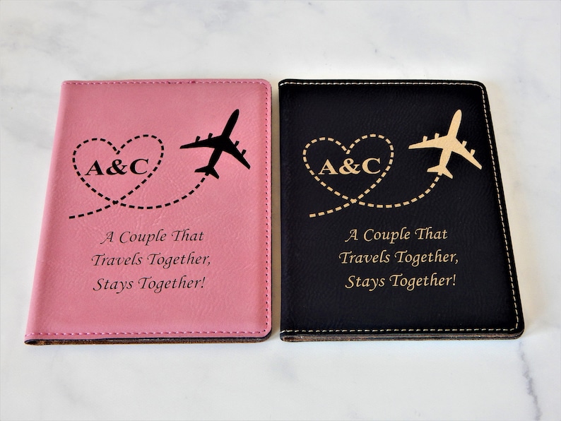 May include: Two passport holders, one pink and one black, with a gold airplane and heart design. The text "A Couple That Travels Together, Stays Together!" is engraved on both holders.