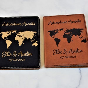 May include: Two passport covers with a world map design. One cover is black with a gold world map and the other is brown with a black world map. Both covers have the text "Adventure Awaits" and "Ellie & Austin 07-02-2021" engraved on them.