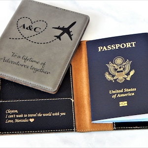 May include: A gray and black passport holder with a brown leather trim. The front cover has a heart with the initials "A&C" and a plane with a dotted line trail. The text "To a lifetime of Adventures together" is engraved on the front cover. The back cover has the text "Clayton, I can't wait to travel the world with you Love, Mercedes".