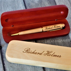 May include: A light-colored wooden pen with gold accents and the engraved name "Richard Holmes" rests inside a red wooden pen case. The matching pen case is closed, also engraved with the name. The text "GREAT ENGRAVED GIFTS" is visible.
