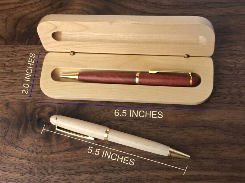 May include: A dark reddish-brown wooden pen with gold-tone accents rests inside a light-colored wooden case measuring 6.5 inches by 2.0 inches. A second light-colored wooden pen with gold-tone accents measures 5.5 inches in length.