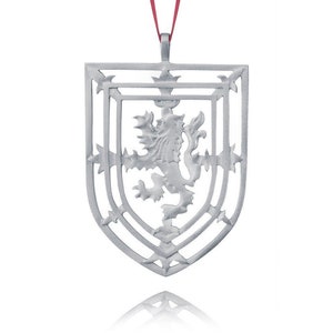 Peut inclure: Une décoration argentée en forme de bouclier avec un lion rampant à l'intérieur. Le bouclier est décoré d'un motif géométrique et est doté d'un ruban rouge attaché au sommet.