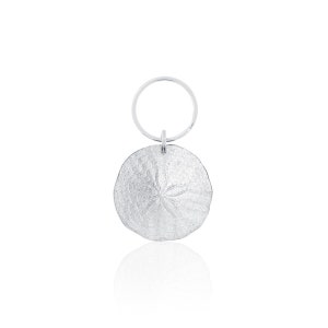 May include: Silver key chain with a sand dollar charm. The charm is round and has a detailed design of a sand dollar.