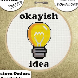Könnte beinhalten: Kreuzstichmuster mit einer gelben Glühbirne und den Worten "okayish idea" in Schwarz. Das Design befindet sich in einem hölzernen Stickrahmen. Zusätzlicher Text enthält "Cross Stitch Pattern", "PDF Digital Download" und "Custom Orders Available".