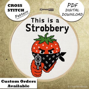 May include: A cross-stitch pattern in a wooden hoop features a red strawberry with a black bandana and a gun, with the text "This is a Strobbery." The design is a digital PDF download. The words "Cross Stitch Pattern" and "Custom Orders Available" are also visible.