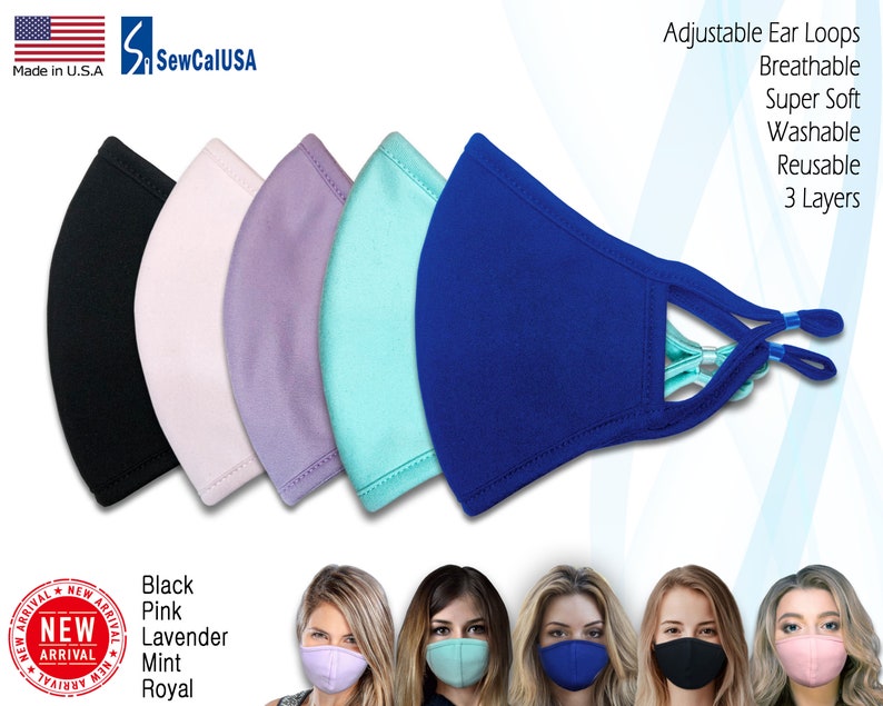 Op de afbeelding: Vijf gezichtsmaskers in verschillende kleuren: zwart, roze, lavendel, mint en koninklijk blauw. De maskers zijn gemaakt van zacht, ademend materiaal en hebben verstelbare oorlussen. De tekst "SewCalUSA" en "Made in U.S.A." is zichtbaar in de linkerbovenhoek van de afbeelding. De tekst "Adjustable Ear Loops", "Breathable", "Super Soft", "Washable", "Reusable" en "3 Layers" is zichtbaar in de rechterbovenhoek van de afbeelding. De tekst "Black", "Pink", "Lavender", "Mint" en "Royal" is zichtbaar in de linkerbenedenhoek van de afbeelding. De tekst "NEW ARRIVAL" is zichtbaar in een rode cirkel in de linkerbenedenhoek van de afbeelding.