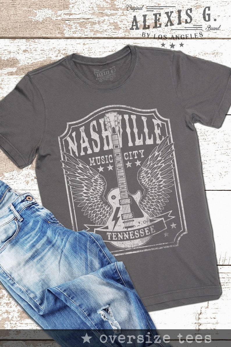 May include: A charcoal grey t-shirt featuring a vintage-style graphic of a guitar with wings. The graphic reads "Nashville Music City Tennessee" and has a distressed look.