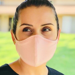 Op de afbeelding: Een persoon draagt ​​een lichtroze gezichtsmasker. Het masker is gemaakt van een zachte, ademende stof en heeft een gecontourde vorm voor een comfortabele pasvorm.